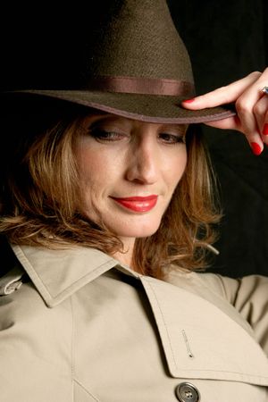 A beautiful woman in a trenchcoat and fedora hat, looking behind her in a secretive way.