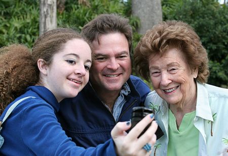 A teen girl takes a picture of herself, her father, and her grandmother with her new camera phone.の写真素材