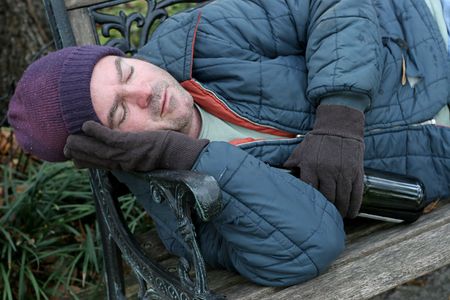 A homeless man asleep on a park bench with a bottle of wine in his hand.の写真素材