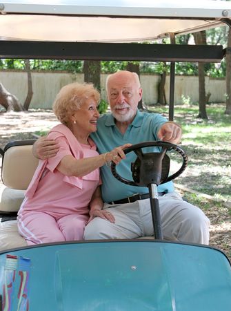 A senior couple riding in a golf card.  She is steering and he is pointing where to go.の写真素材