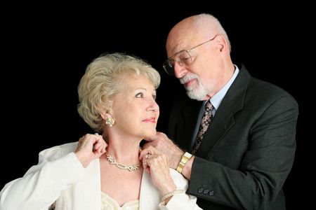 A horizontal view of a senior man fastening his wife's necklace as they prepar for an evening out.