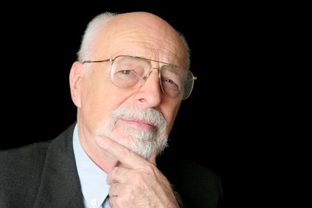 A skeptical looking, intelligent senior man over a black background.