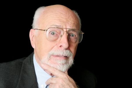 A distinguished senior man with a scared expression over a black background.の写真素材