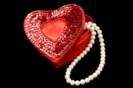 A red satin heart shaped box filled with pearls, isolated on a black background.の写真素材