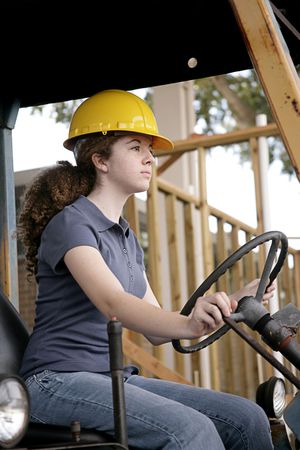A female construction worker driving heavy equipment.  Vertical view.