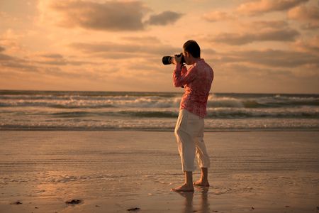 A photographer taking a picture of the sun setting over the ocean.