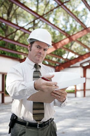 A skeptical looking construction inspector going over his notes and pointing out problems.の写真素材