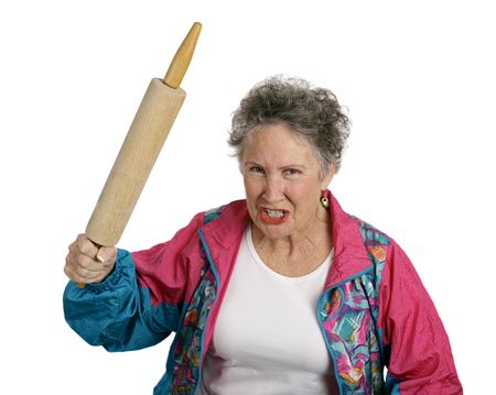 A very angry senior lady holding a rolling pin and threatening to whack someone with it (her husband?).  Isolated on white.の写真素材