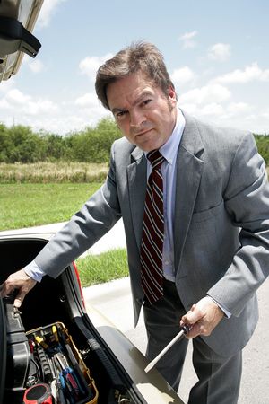 A businessman rooting in his trunk for tools to repair his broken down car.の写真素材