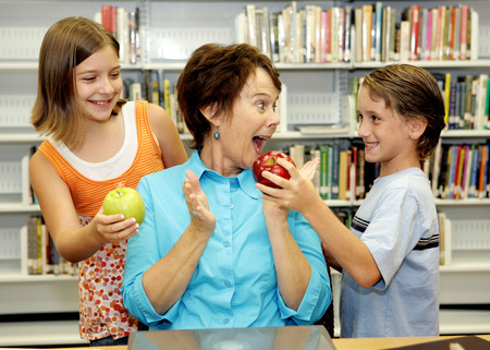 Two students giving apples to their favorite teacher.  She is very surprised and happy.の写真素材