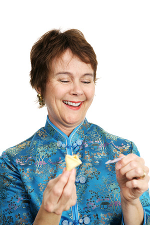 A pretty, mature woman dressed in a silk chinese blouse opening a fortune cookie and laughing at the fortune inside.  の写真素材