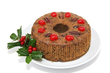 Beautiful Christmas fruitcake garnished with cherries, pecans and a sprig of holly.  Isolated on white background.の写真素材