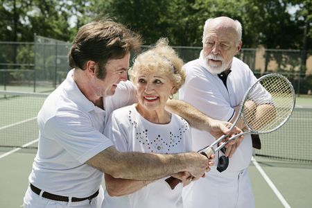 Senior lady taking tennis lessons from a handsome pro while her husband looks on jealously.  