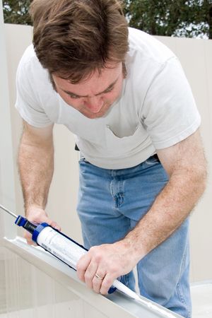 Handyman using a caulking gun to caulk a window.  の写真素材