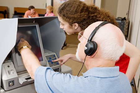 Poll worker explains the new touch screen voting machine to senior voter.  