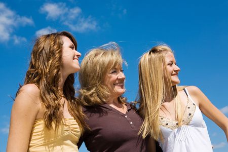 Beautiful grandmother & granddaughters laughing in profile against a blue sky.  
