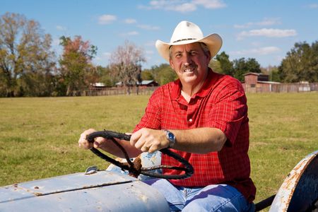 Handsome middle-aged cowboy riding his tractor through his fields.の写真素材