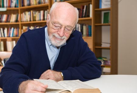 Senior man enjoys a good book in the library.  Horizontal view with room for text.  の写真素材