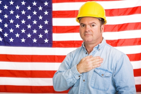 Patriotic american worker with his hand over his heart in front of the US flag.  Photographed in front of flag, not composite image.の写真素材