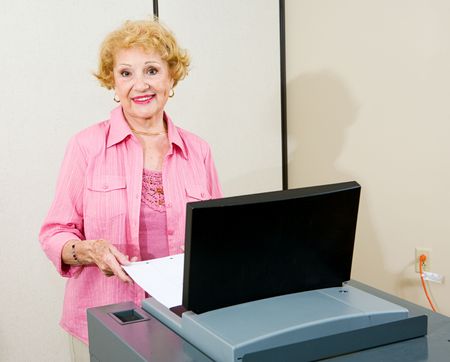 Senior woman feeding her ballot into a new optical scan voting machine.  Authentic image shot at...