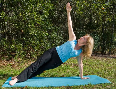 Beautiful fit woman in her sixties doing the side staff yoga asana, outdoors in a natural setting.  の写真素材