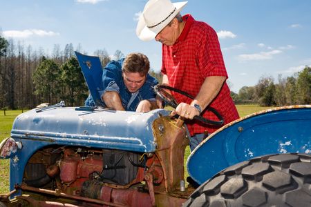 Farmer and ranch hand work on repairing the old tractor together.  の写真素材