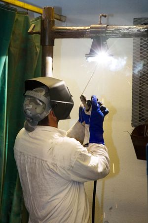 Welder in a metal shop welding overhead.  Actual welder working according to industry code and...