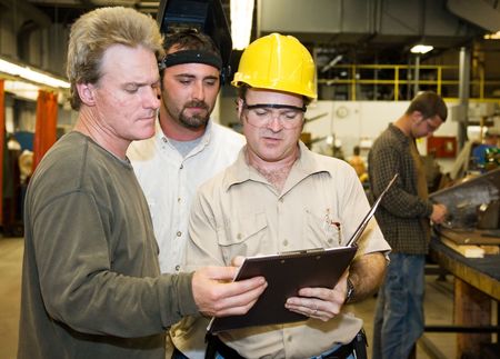 Factory worker and foreman discuss inspection report with auditor.  