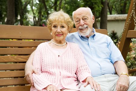 Happy, attractive senior couple relaxing together on a swing in the park.