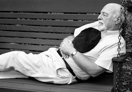 Black and white image of senior man taking a nap on a park swing.  の写真素材