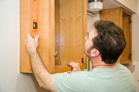 Carpenter installing solid maple kitchen cabinets, using a level to check his work.の素材 [FY3103766954]