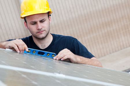Worker installing solar panels uses a level to check that the angle is right.  の写真素材