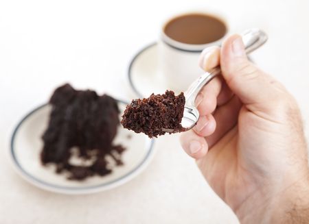 Closeup of a piece of chocolate cake on a fork in a man's hand.  Shallow depth of fieldの写真素材