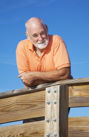 Portrait of a handsome, fit senior man leaning on a wood railing.  の写真素材