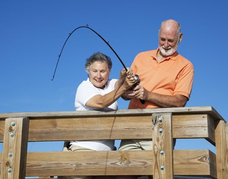 Senior couple fishing, working together to reel in a big fish.  の写真素材