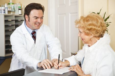 Doctor helps senior woman fill out paperwork in his office.  の写真素材