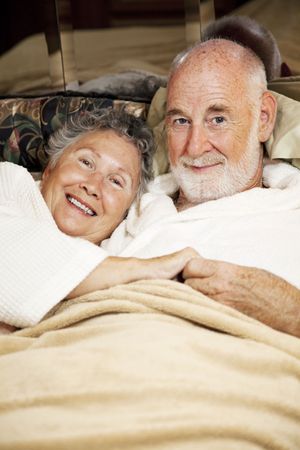 Happy senior couple snuggling in bed.  Vertical view.の写真素材