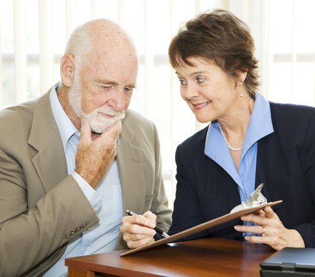 Senior man reading and thinking about a contract while eager businesswoman encourages him to sign.  の写真素材