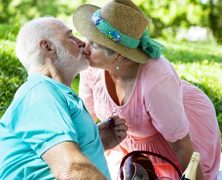 Senior couple on a picnic, kissing in the park.  の写真素材