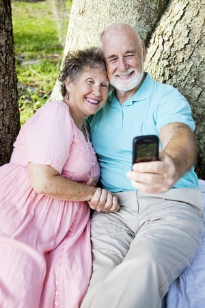 Senior couple e-mailing a picture of themselves to their kids, using a cellphone.  の写真素材