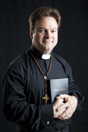 Portrait of a priest with a rosary and a bible.  Dramatic lighting over black background.  の写真素材