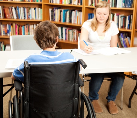Disabled student in the school library, studying with a classmate.  Focus on the boy in the wheelchair.  の写真素材