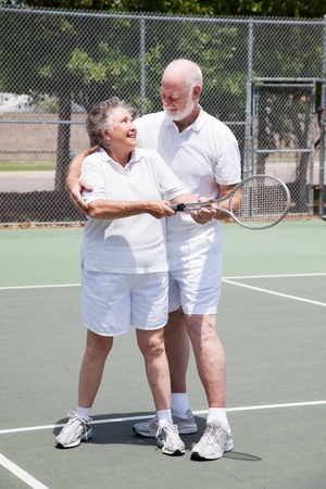 Pretty senior woman gets a tennis lesson from her handsome husband.  の写真素材
