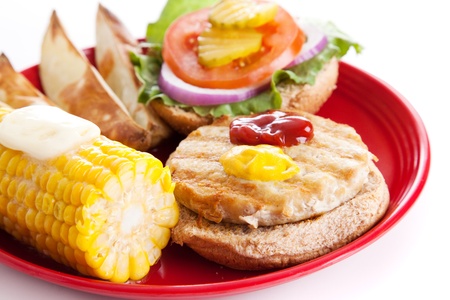 Healthy turkey burger on a whole grain bun, with baked potato wedges and corn on the cob.  Isolated on white.  の写真素材