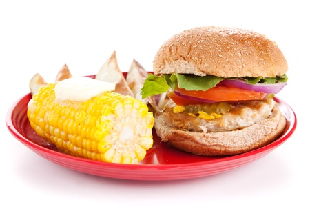 Healthy turkey burger, corn on the cob, and baked potato wedges on white background.  の写真素材