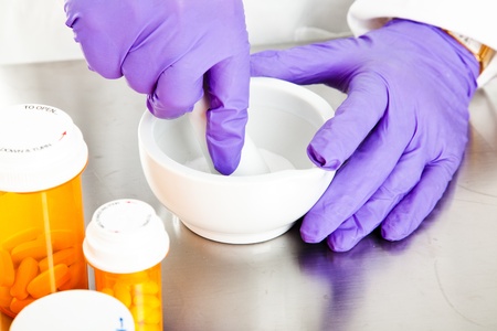 Closeup view of a pharmacist's hands, using a mortar and pestle.  
