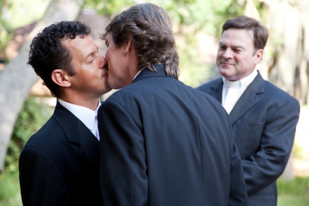 Wedding of handsome gay male couple.  The grooms kiss as the minister looks on.  の写真素材