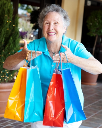 Senior woman addicted to shopping, holding up a handful of bags.  の写真素材