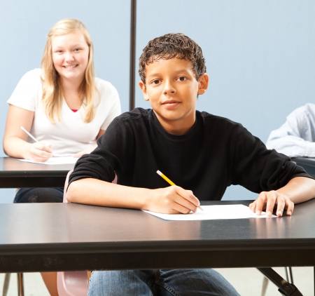 Handsome adolescent boy in school classroom, sitting at desk.  の写真素材