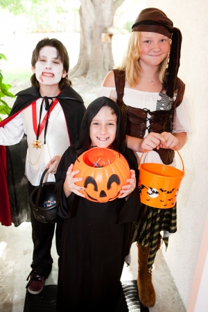 Three kids in Halloween costumes going trick or treating door-to-door.  Focus on little boy in front.  の写真素材
